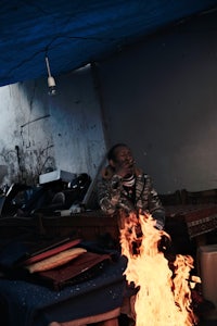 a man sits in front of a fire in a tent