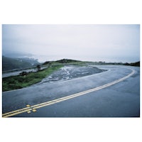 a curvy road on a rainy day with the ocean in the background